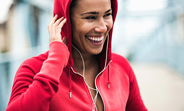 Hooded woman wearing headphones in a red jacket smiling