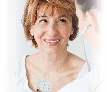 female patient smiles while male doctor listens to her heart